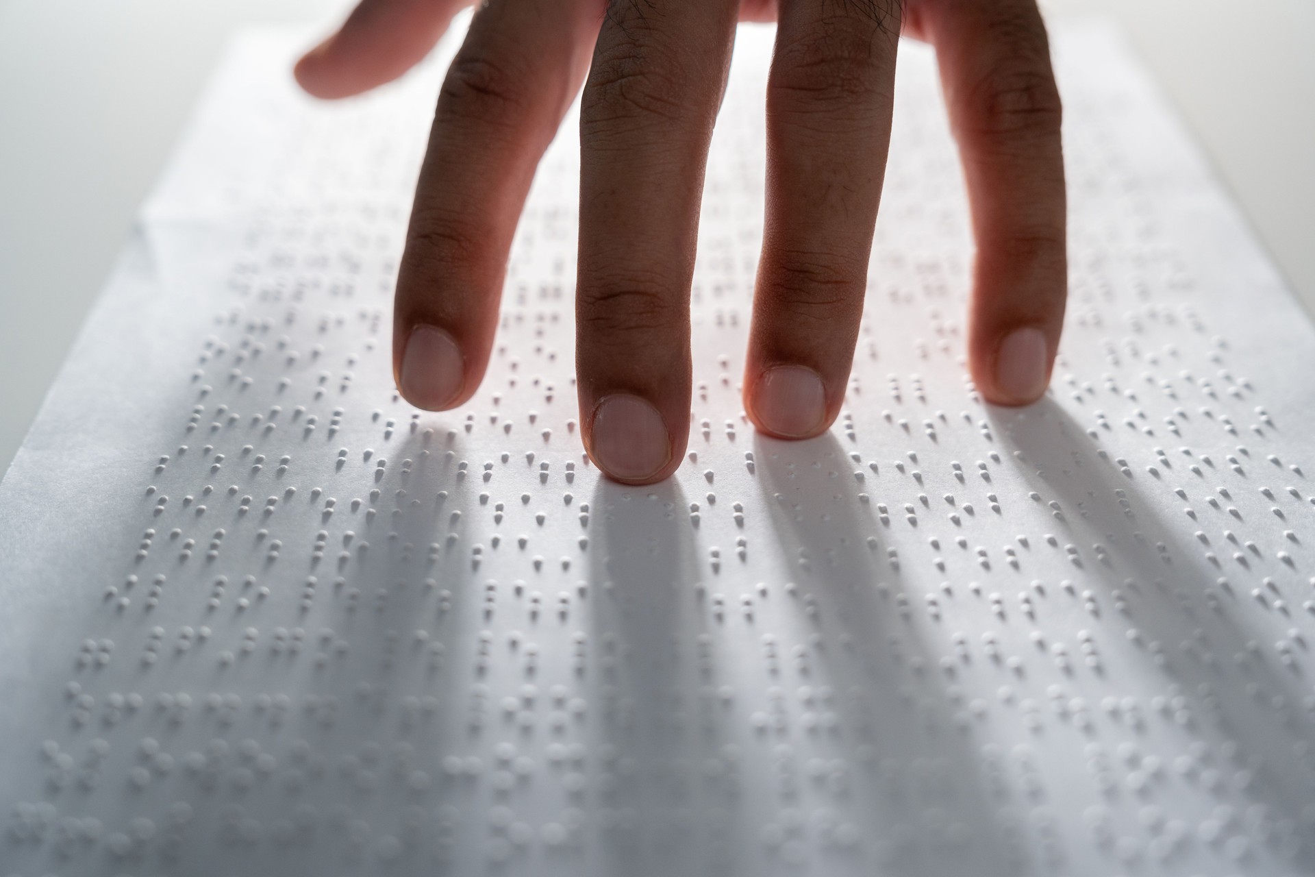 Hand of a blind person reading some braille text on page paper to learn. Finger of blind student touching the braille alphabet Code on sheet.