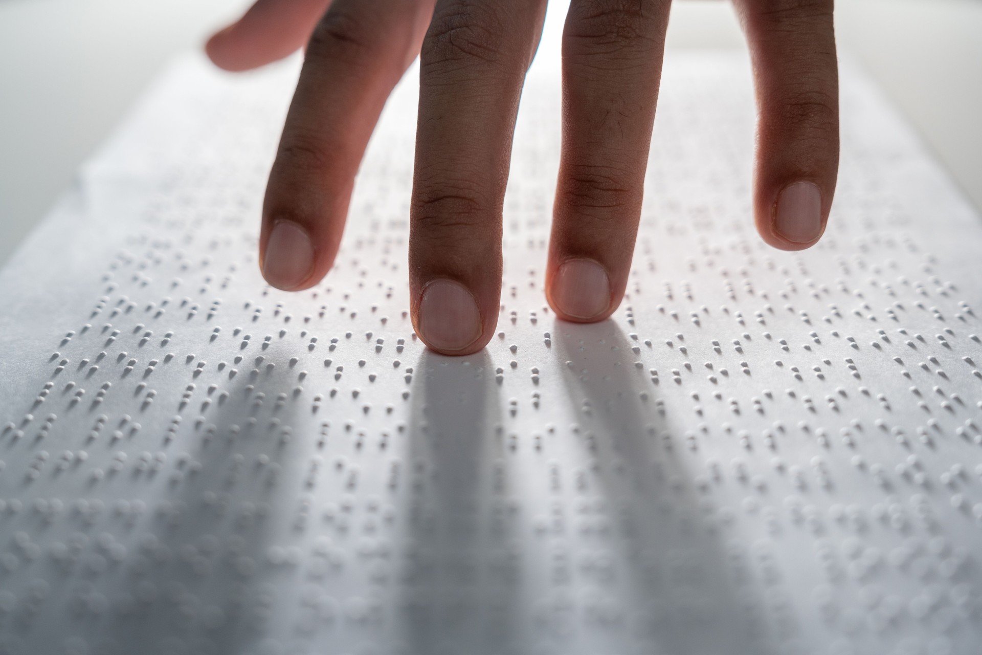 Hand of a blind person reading some braille text on page paper to learn. Finger of blind student touching the braille alphabet Code on sheet.
